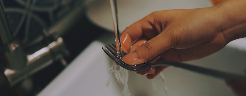 Person rinsing a fork under water