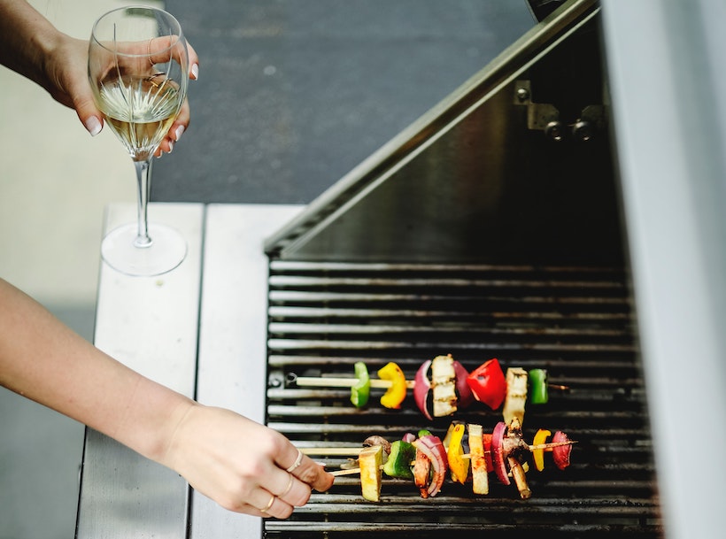 Woman grills kabobs with wine in hand
