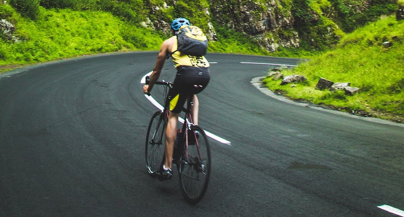 Man biking on left side of road around corner