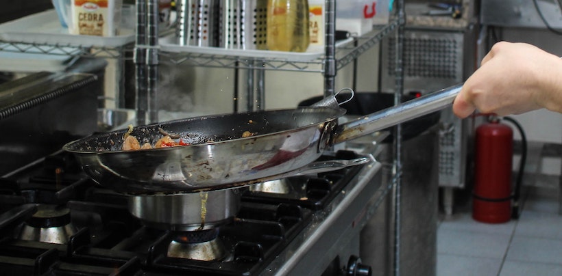 Stainless steel frying pan and a man's hand in a commercial kitchen