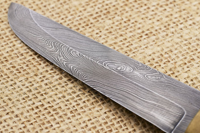 Traditional handmade Finnish knife with the abstract wave pattern of damascus steel over an old sack background.
