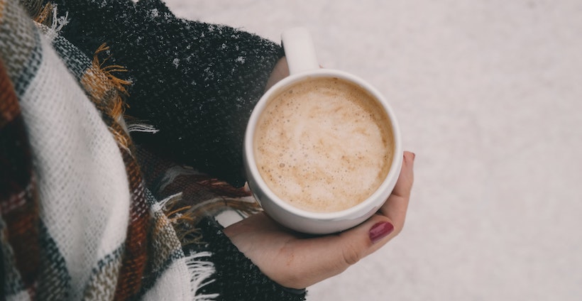 Lady in winter clothes holds a hot coffee