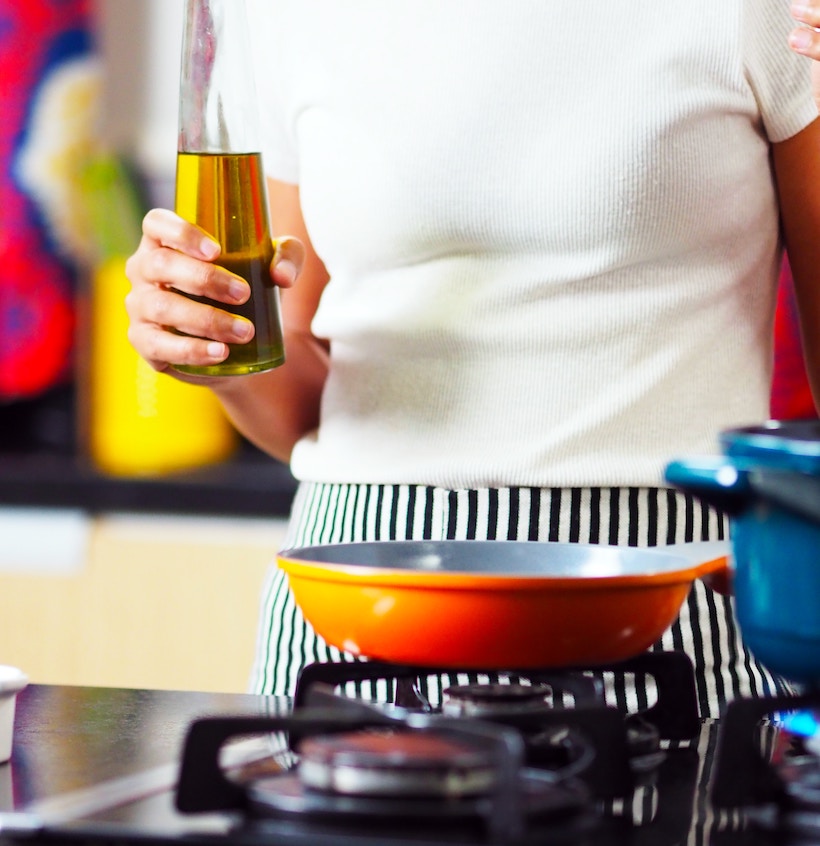 Lady holding olive oil next to gas grill with orange pan