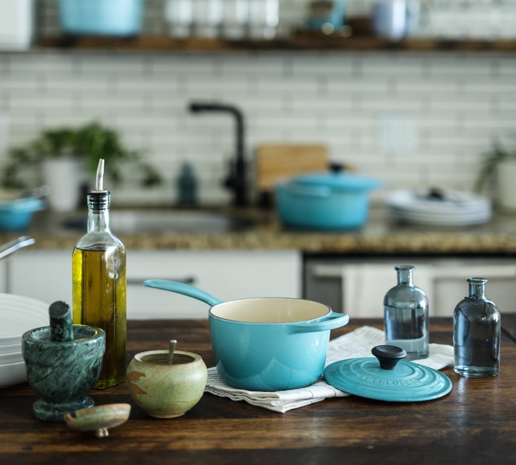 Olive oil next to blue cast iron pan kitchen in background