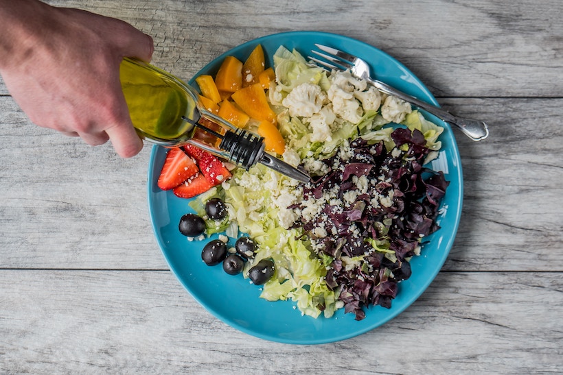 Man pouring olive oil on a complicated salad