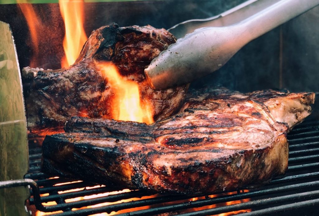 Steak tongs used to flip a steak over a flame on grill