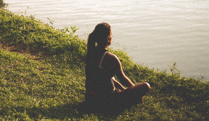 Woman meditating on the grass looking at a pond