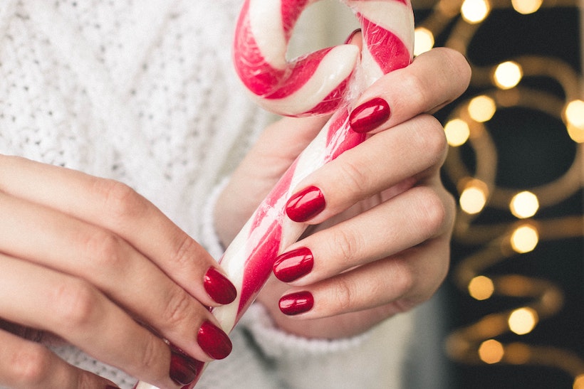 Lady holds giant candy cane and has bright red matching manicure