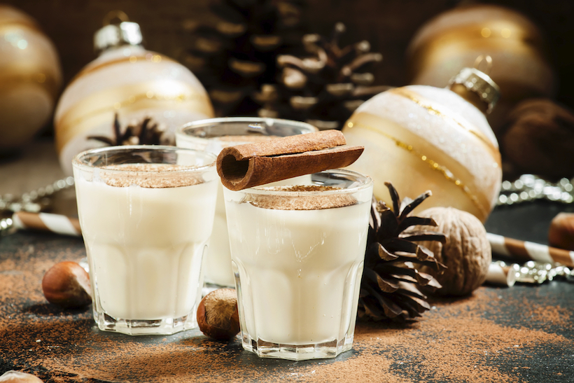 Eggnog with milk, cinnamon, grated nutmeg, decorated with fir cones, beads, nuts and Christmas balls, selective focus