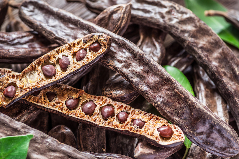 Carob pods, beans, and leaves on a wooden table