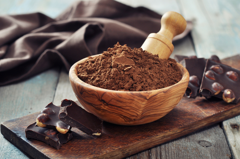Carob powder in bowl with carob pieces on wooden board