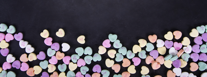 Conversation hearts on a black chalkboard background.