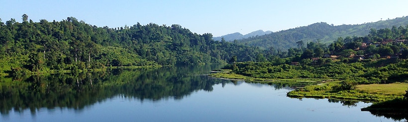 Lake with mountains, trees, sky, and some houses in distance