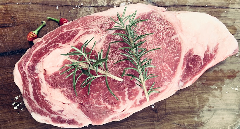 Red meat on cutting board with sprigs of herbs