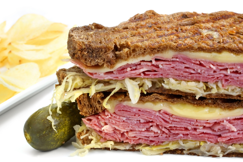 Reuben sandwich, with pastrami, sauerkraut, melting Swiss cheese on dark rye bread.  With dill pickle and potato crisps.
