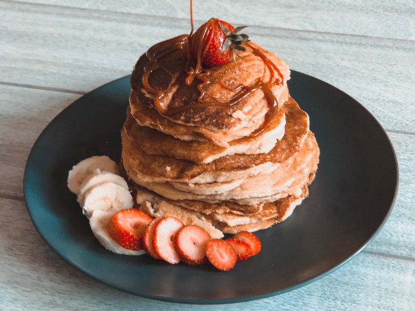 Stack of pancakes with strawberries and bananas and caramel syrup