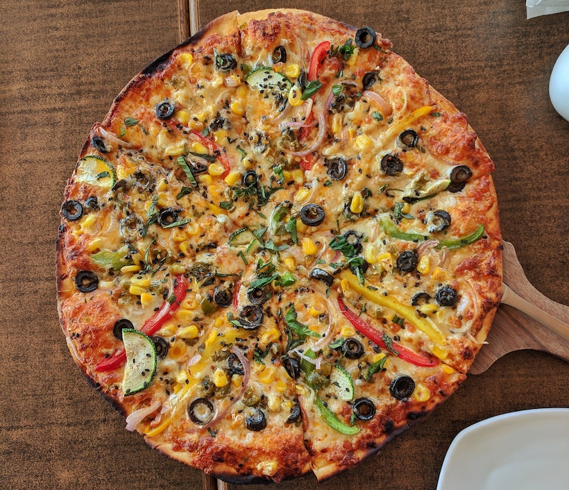 Paddle under a pepper, olive, herb, and other vegetable thin crust pizza