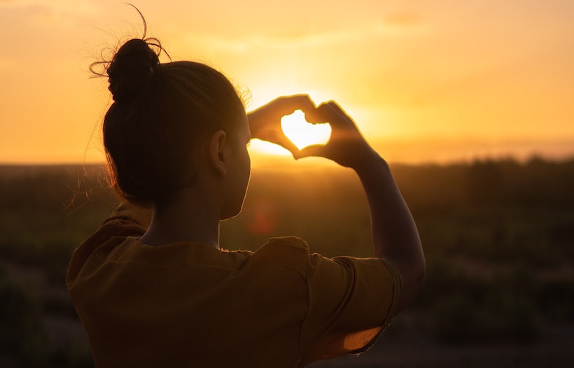 A woman captures the setting sun in her hands shaped like a heart