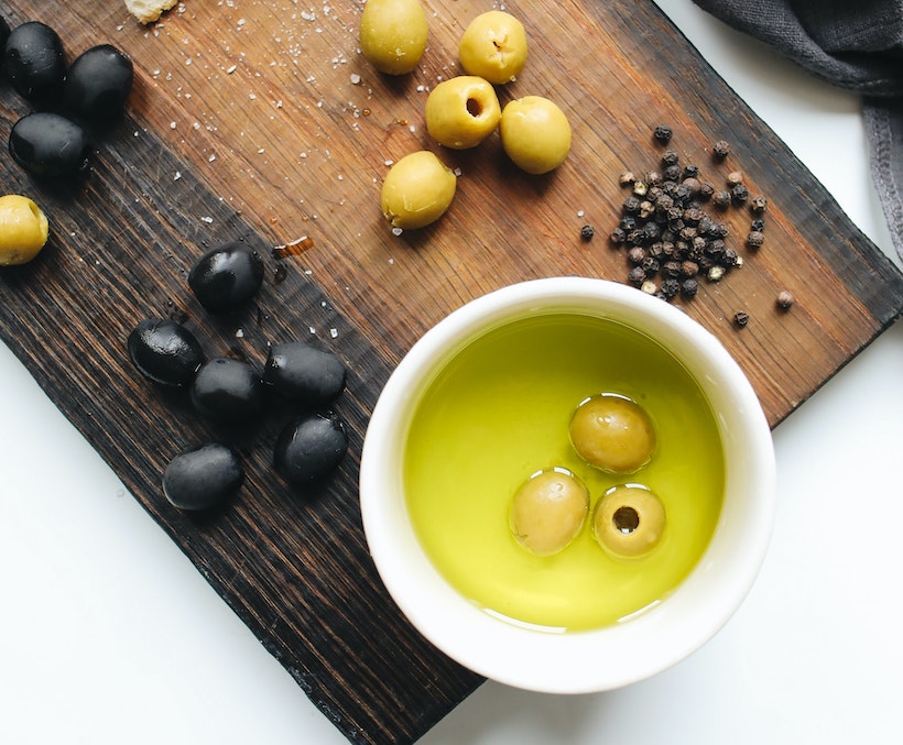 Olives, peppercorns, and olive oil on a cutting baord