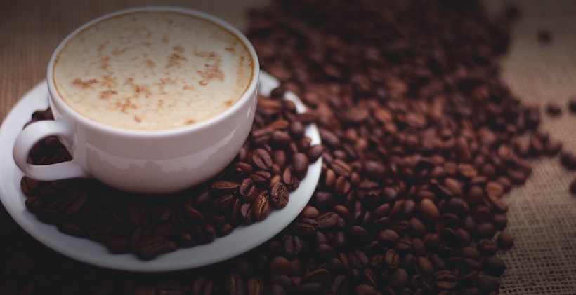 Coffee cup with milk next to whole coffee beans