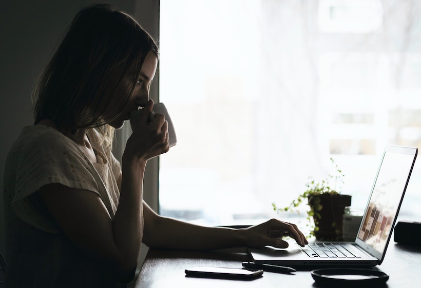 A lady drinks coffee while scrolling on a computer