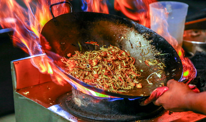 Lots of flame in a wok on an open burner with noodles