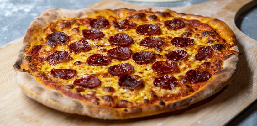 Angled shot of pepperoni pizza on wooden server