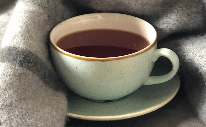 A coffee mug in bed under a blanket