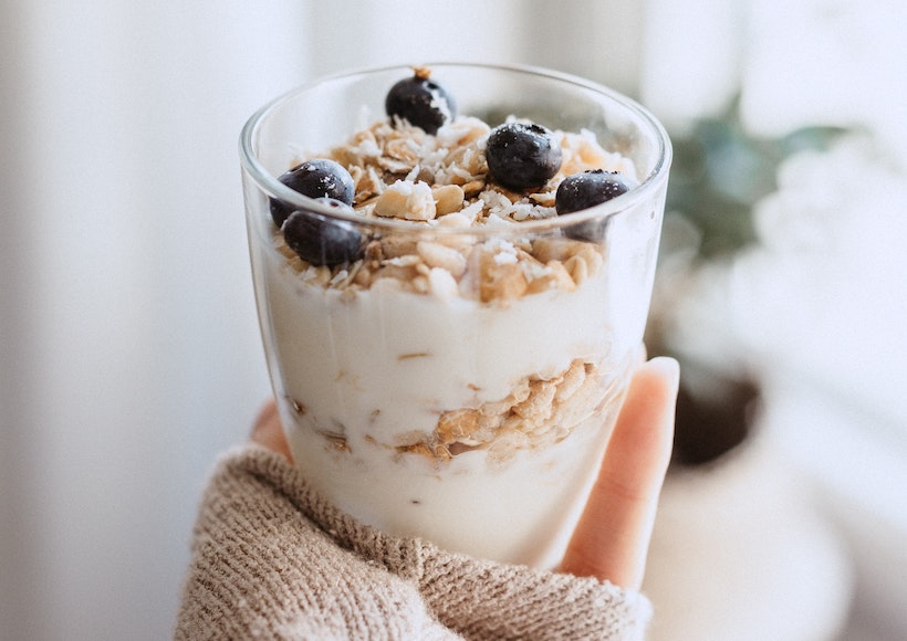 Lady holding a cup of yogurt with granola and blueberries