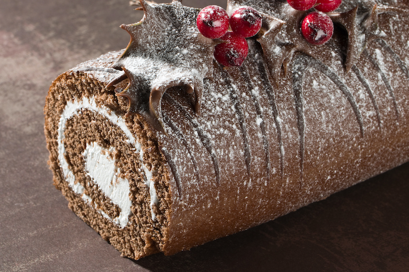 Close up of Christmas Yule chocolate log decorated with dipped holly leaves and berries, dusted with icing sugar