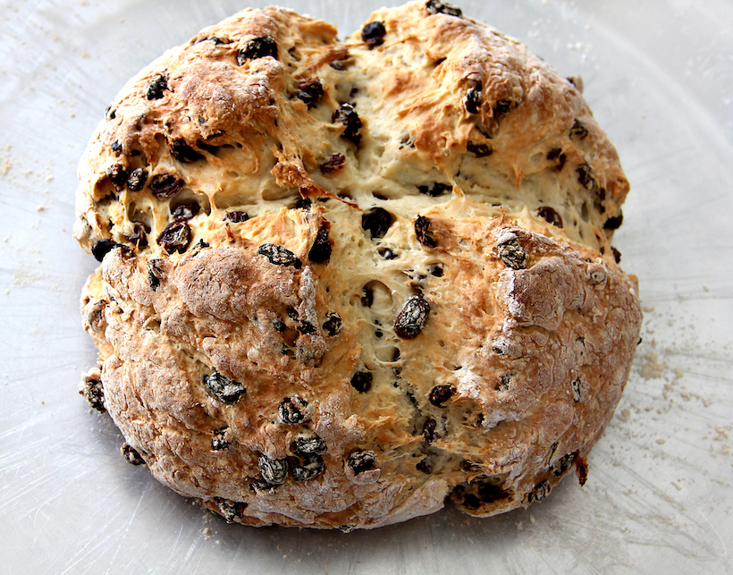 A loaf of Irish Soda Bread with raisins on baking sheet.