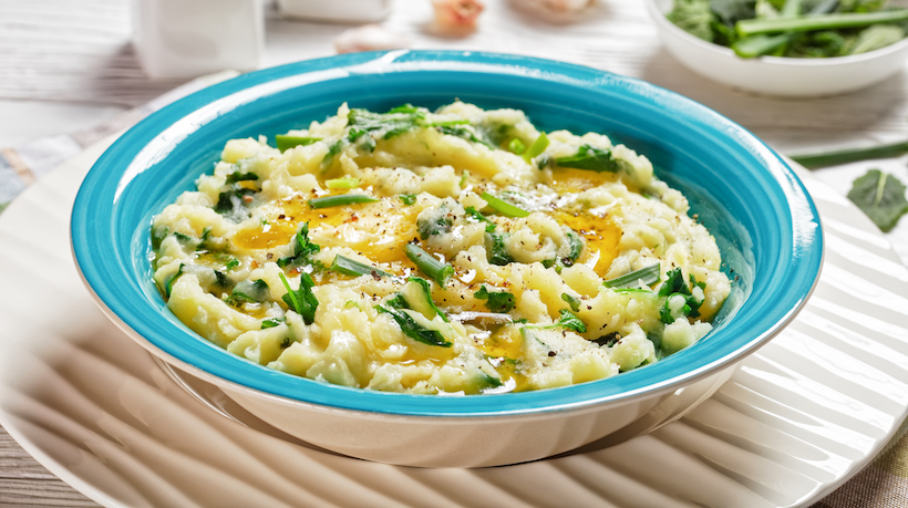 Irish colcannon traditional potato mash with kale, garlic, melted butter and spring onion served on a blue bowl, white counter plate